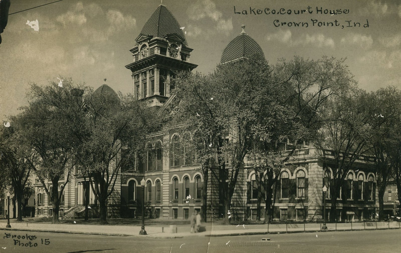 Sepia postcard of the Lake County Courthouse in Crown Point with twin domed towers behind a row of trees